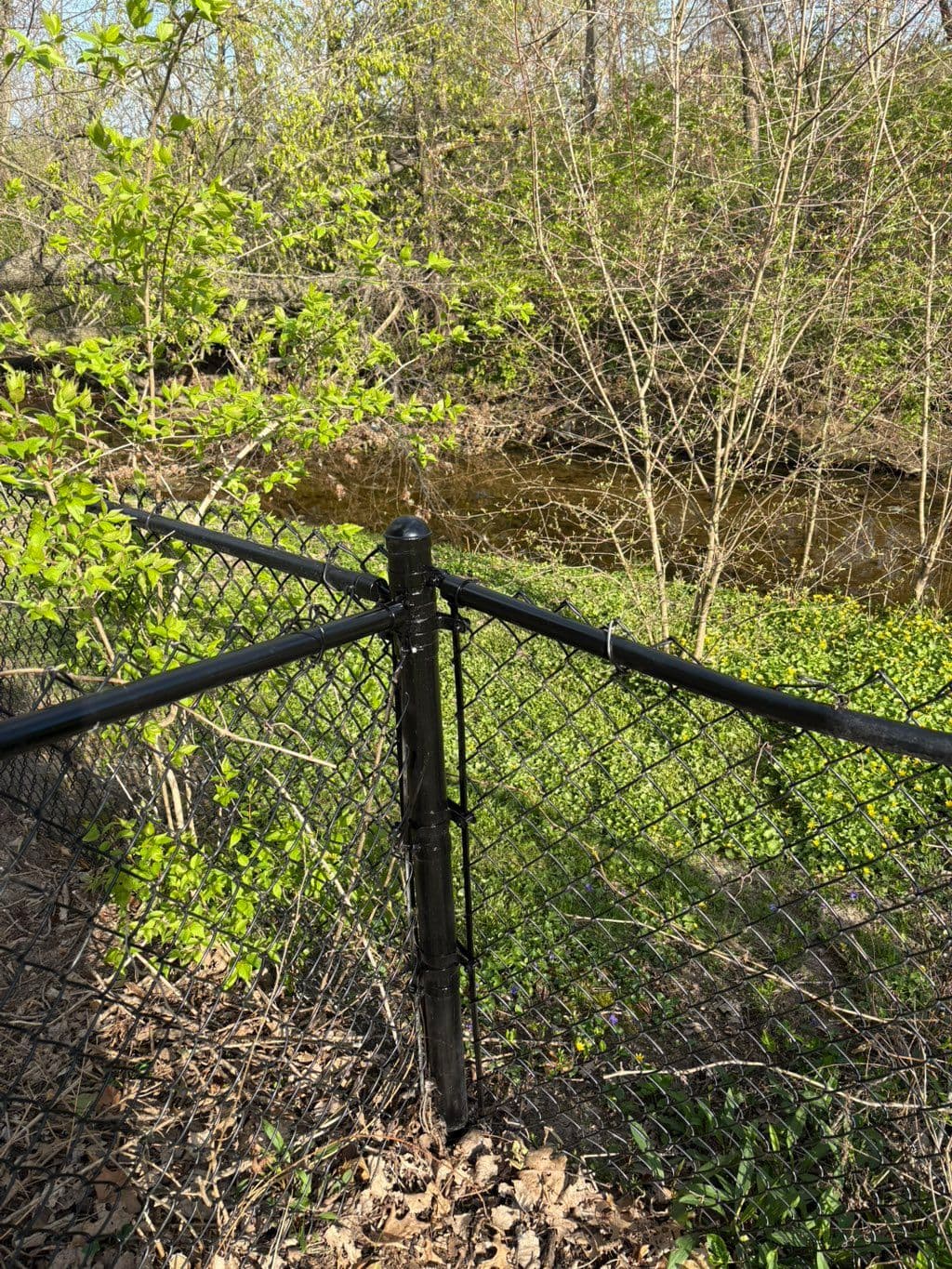 Black chain link fence corner post installed along wooded creek bank