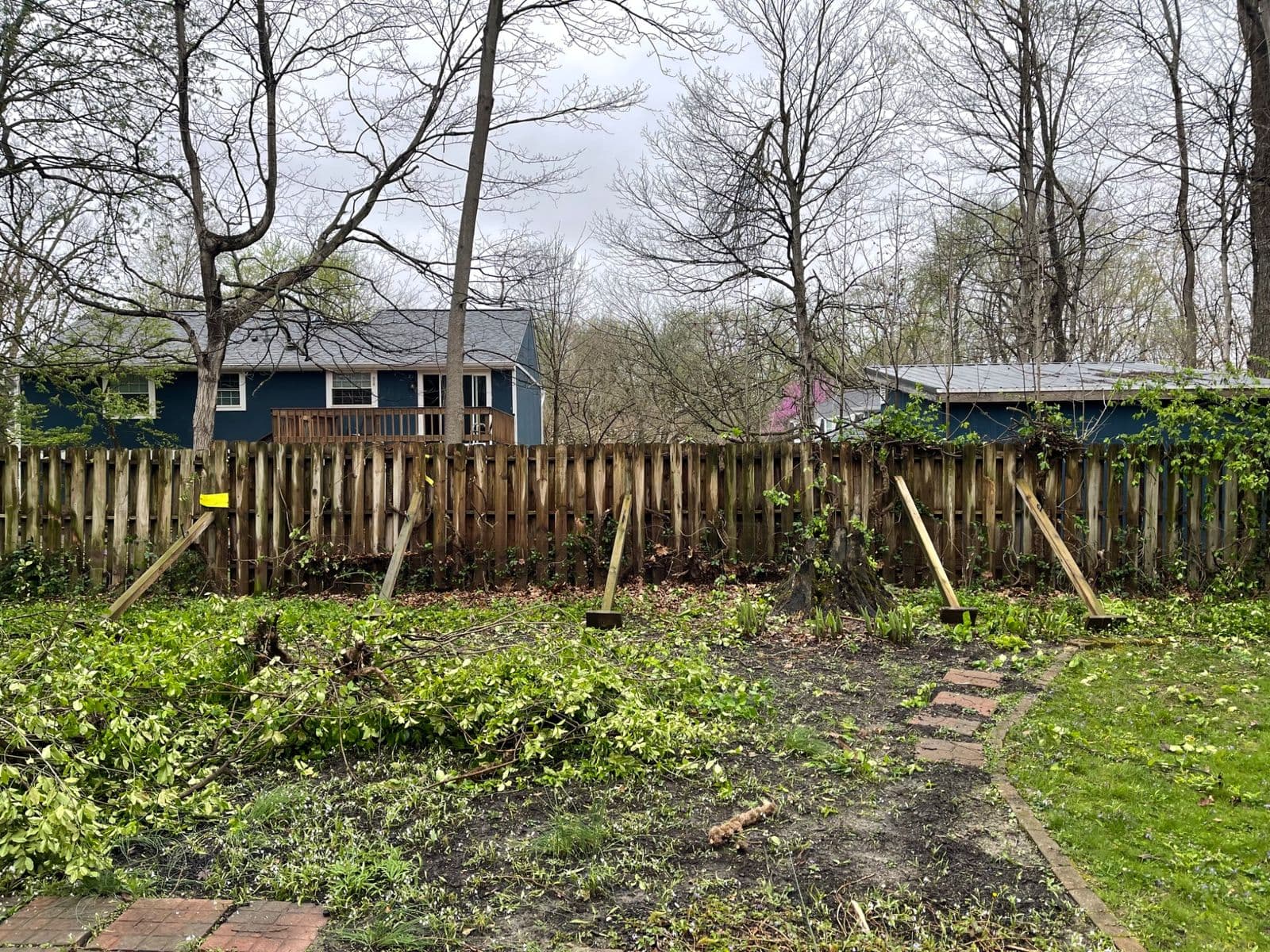 Storm-damaged wood privacy fence propped with braces, debris scattered in yard