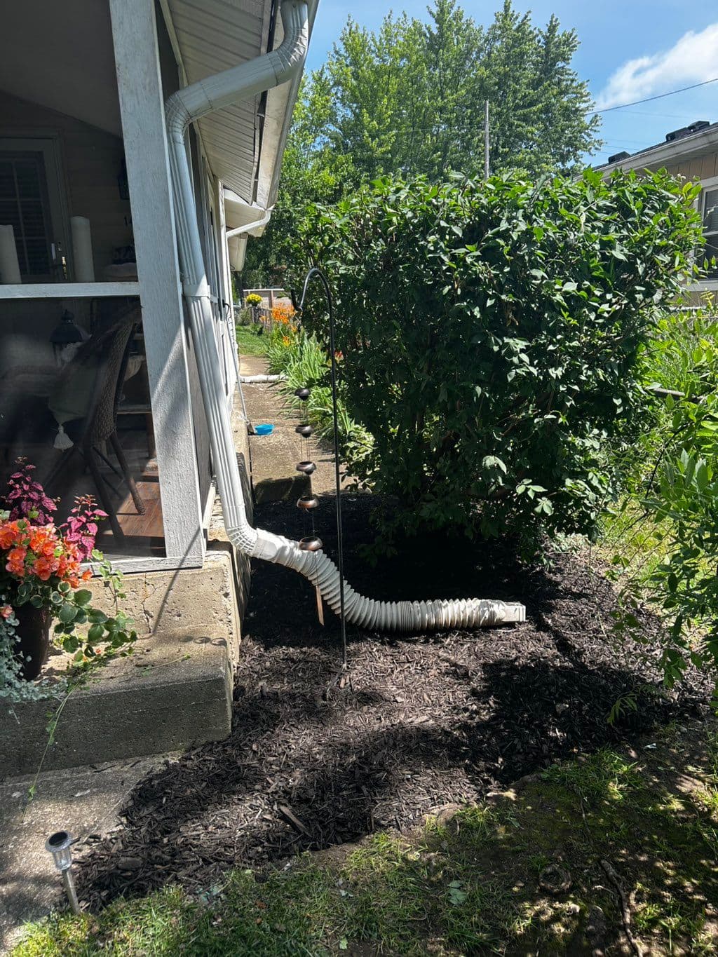 Dark mulch laid along house foundation beside downspout and shrubs